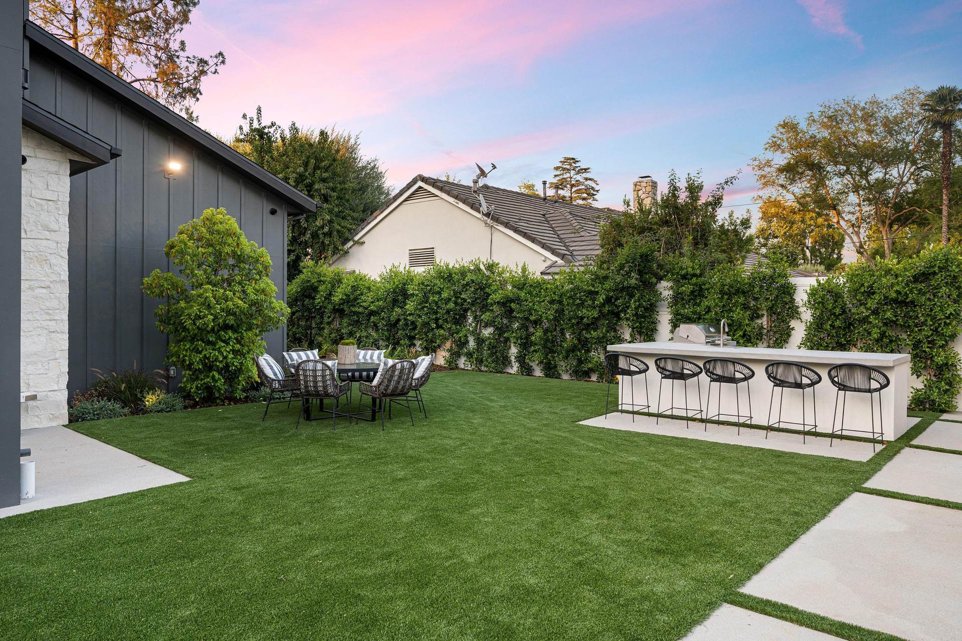 Artificial turf backyard installation in Palm Coast, Florida, with a modern home, outdoor bar, and landscaping at sunset.